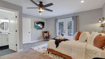 A bedroom with a bed, a ceiling fan, a television, and a view of the outdoors through a window.