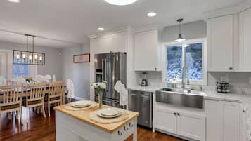 A modern kitchen with white cabinetry, a stainless steel refrigerator, a built-in dishwasher, and a large window with a view of trees.