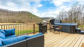 A deck with a grill, hot tub, and seating area overlooking a hilly landscape.
