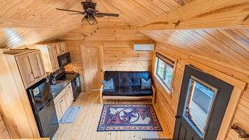 A compact wooden cabin with a kitchenette, a sofa, and a ceiling fan.