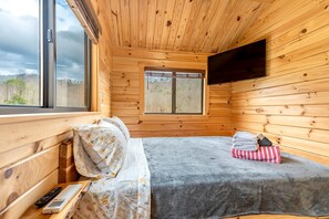 A wooden cabin room with a bed, a window, and a mounted TV.