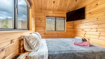 A wooden cabin room with a bed, a window, and a mounted TV.