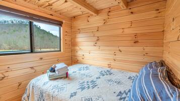 A wooden cabin room with a bed, a window, and a view of a forested hillside.