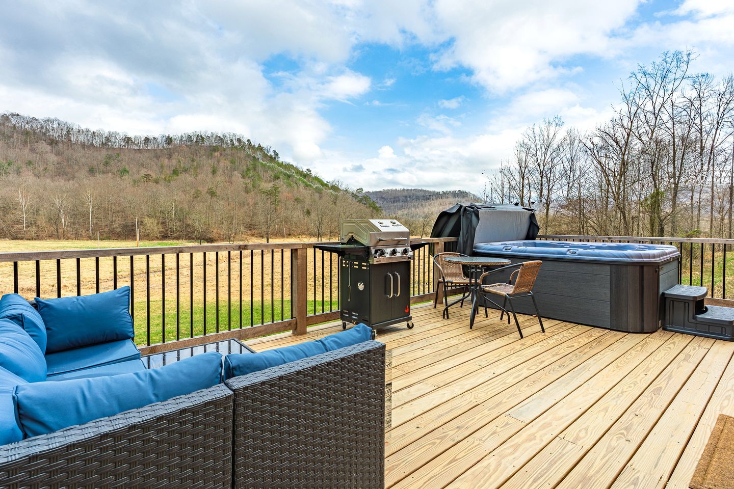 Een terras met een barbecue, jacuzzi en zitgedeelte met uitzicht op een glooiend landschap.