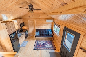 Una cabaña de madera pequeña con kitchenette, un sofá y un ventilador de techo.