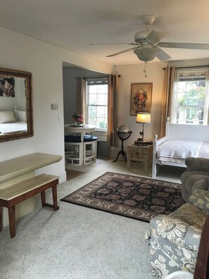 A cozy room with a bed, a desk, a chair, a large mirror, and a ceiling fan.