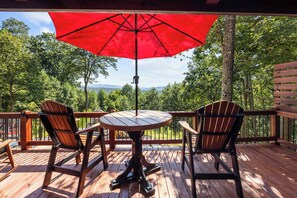 A wooden deck with two Adirondack chairs and a table under a red umbrella, overlooking a forested area. - Heavenly Mountain VIew, Hot Tub, Fire Pit (Blue Ridge)