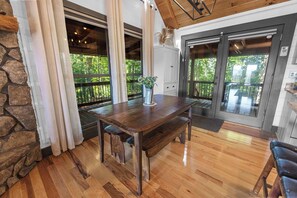 A wooden dining table with benches, a stone wall, and a view of greenery through large windows. - Heavenly Mountain VIew, Hot Tub, Fire Pit (Blue Ridge)