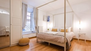 A bedroom with a four-poster bed, a window with curtains, a radiator, and a small bedside table. - Modern Flat in Historic Rome Center (Rome)
