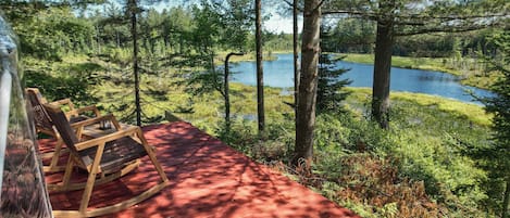 A wooden deck with rocking chairs overlooking a lake surrounded by trees.