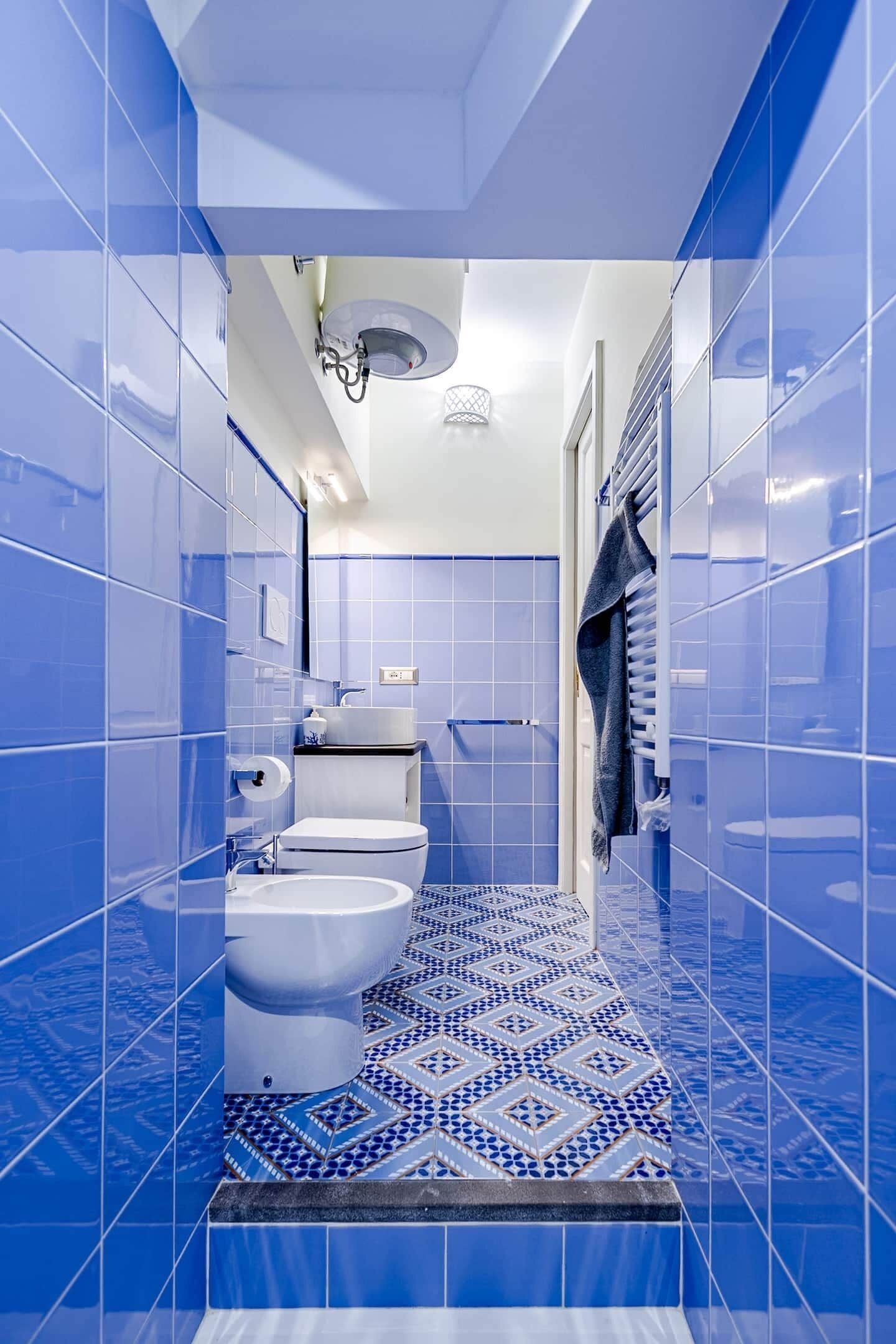 Ein Badezimmer mit blauen Fliesen, einer Toilette, einem Bidet, einem Waschbecken und einem Handtuchhalter.