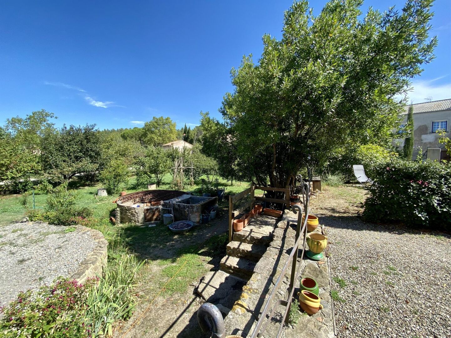A rustic outdoor setting with a wooden structure, possibly a shed, surrounded by greenery and a clear blue sky.
