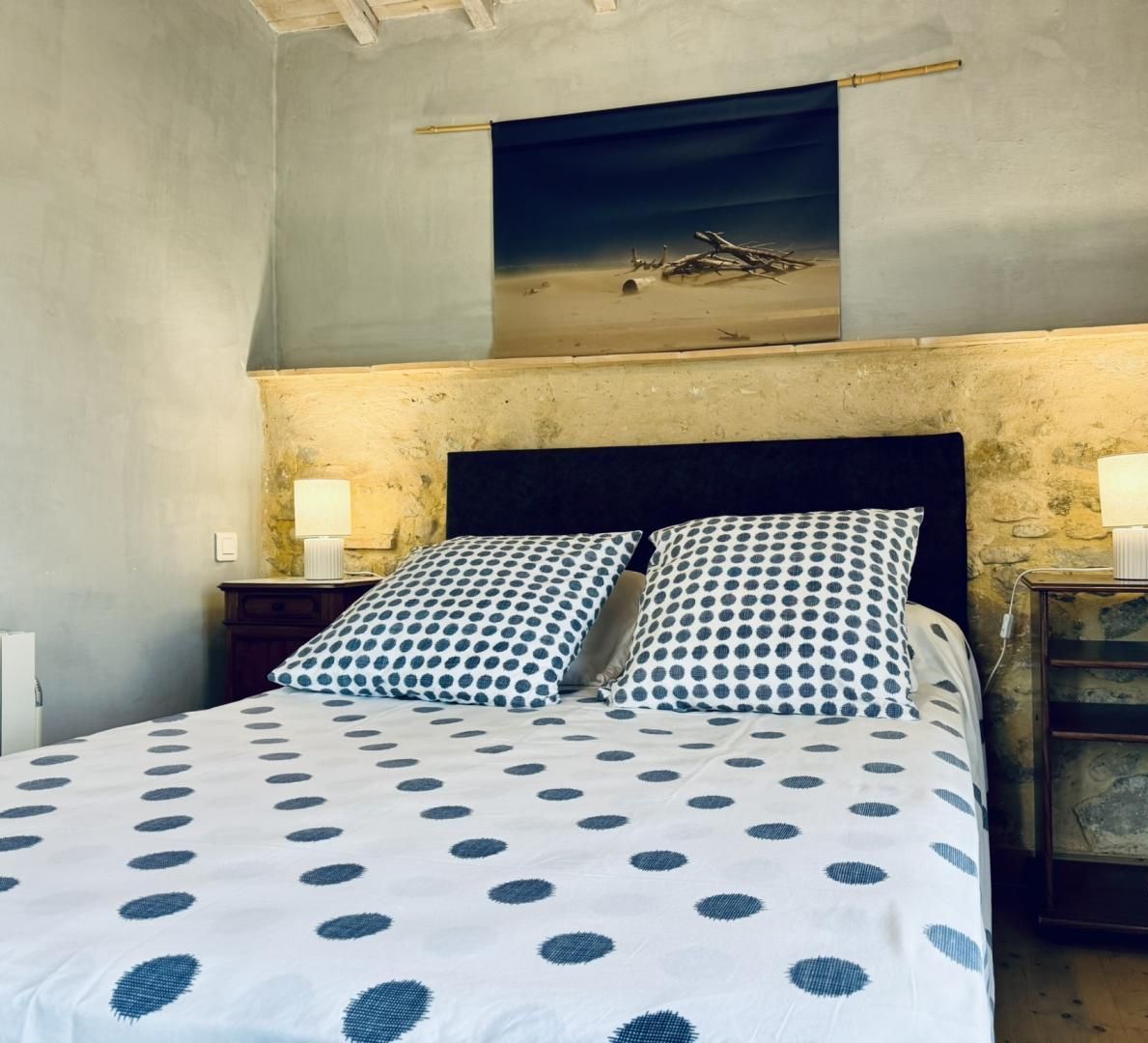 A bedroom with a bed, two nightstands, a painting above the bed, and a logo on the wall.