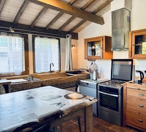 A kitchen with a gas stove, oven, wooden cabinets, and a clock on the wall. - Le Jardin de Marie - TALAIRAN (TALAIRAN)