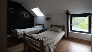 Een kleine, zwak verlichte kamer met twee eenpersoonsbedden, een dakraam en een raam met uitzicht op bomen.