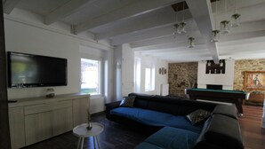 Een ruime woonkamer met een grote flatscreen-tv, een donkergrijze bank en een pooltafel.