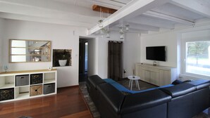 Een moderne woonkamer met een zwarte leren bank, een witte tv-meubel en een groot raam dat natuurlijk licht binnenlaat.