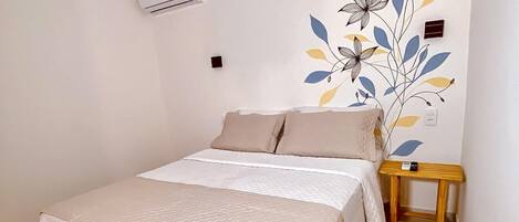 A bedroom with a bed, a nightstand, a wall-mounted air conditioner, and a decorative wall mural.