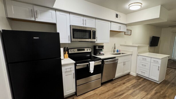 A modern kitchen with white cabinets, stainless steel appliances, and a wooden floor. - Modern Stay Near UAMS, Downtown & Attractions (Little Rock)