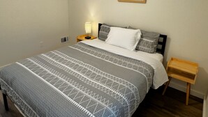 A neatly made bed with a patterned blanket, a bedside lamp, and a small wooden nightstand. - Modern Stay Near UAMS, Downtown & Attractions (Little Rock)