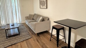 A living room with a sofa, a coffee table, a rug, a framed picture on the wall, and a small table with a stool. - Modern Stay Near UAMS, Downtown & Attractions (Little Rock)