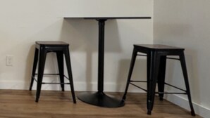 A room with a black round table and two black stools. There is a framed sign on the wall above the table. - Modern Stay Near UAMS, Downtown & Attractions (Little Rock)