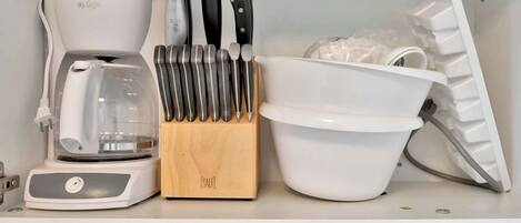 A kitchen with a coffee maker, knife block, and a white bowl.