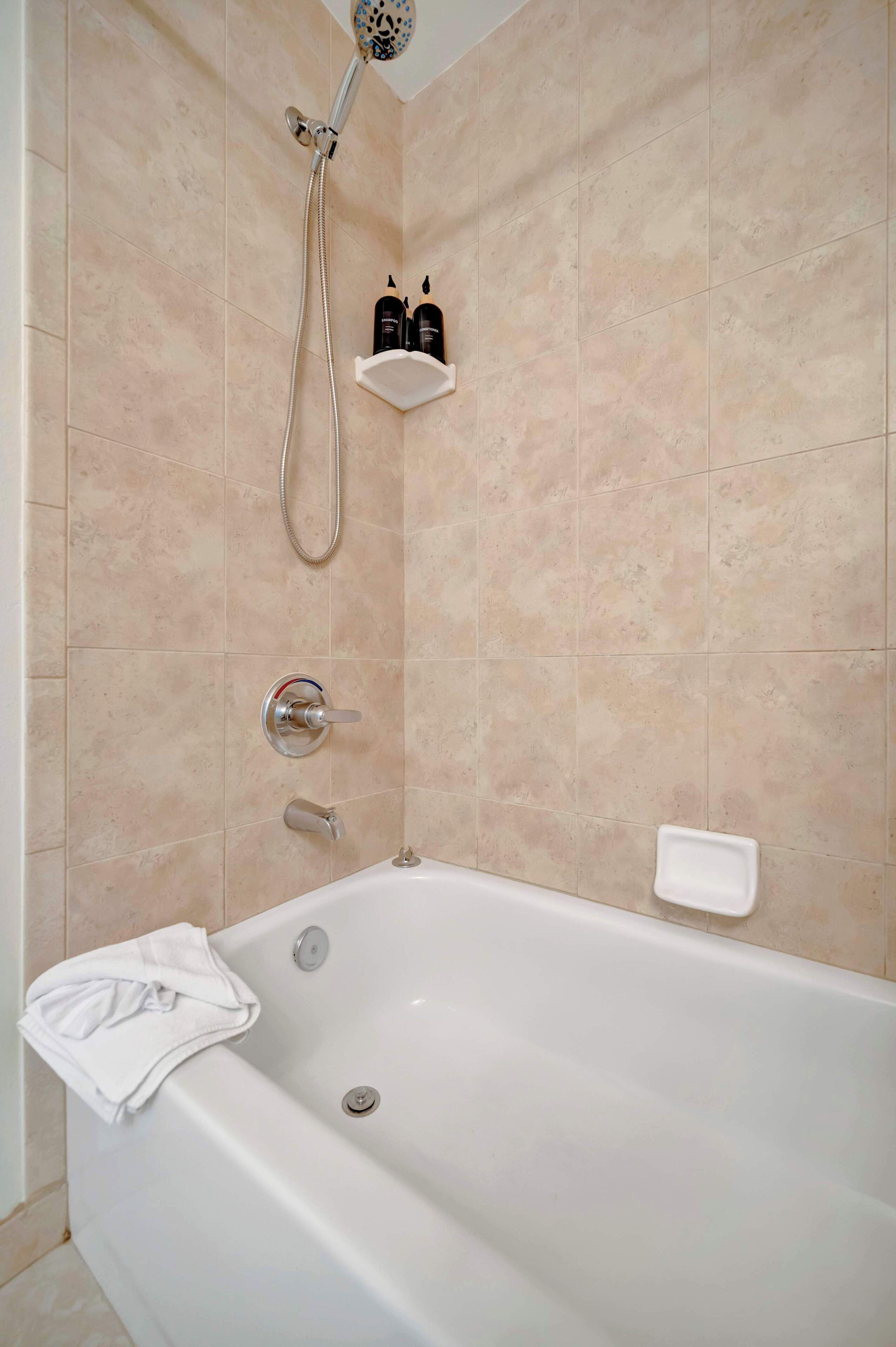 A bathroom with a bathtub, a shower, and a shelf with toiletries.