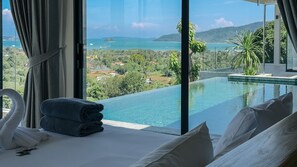 A bedroom with a large window overlooking a pool and a scenic view of a coastal area. - The Salin Seaview Villas (Rawai)