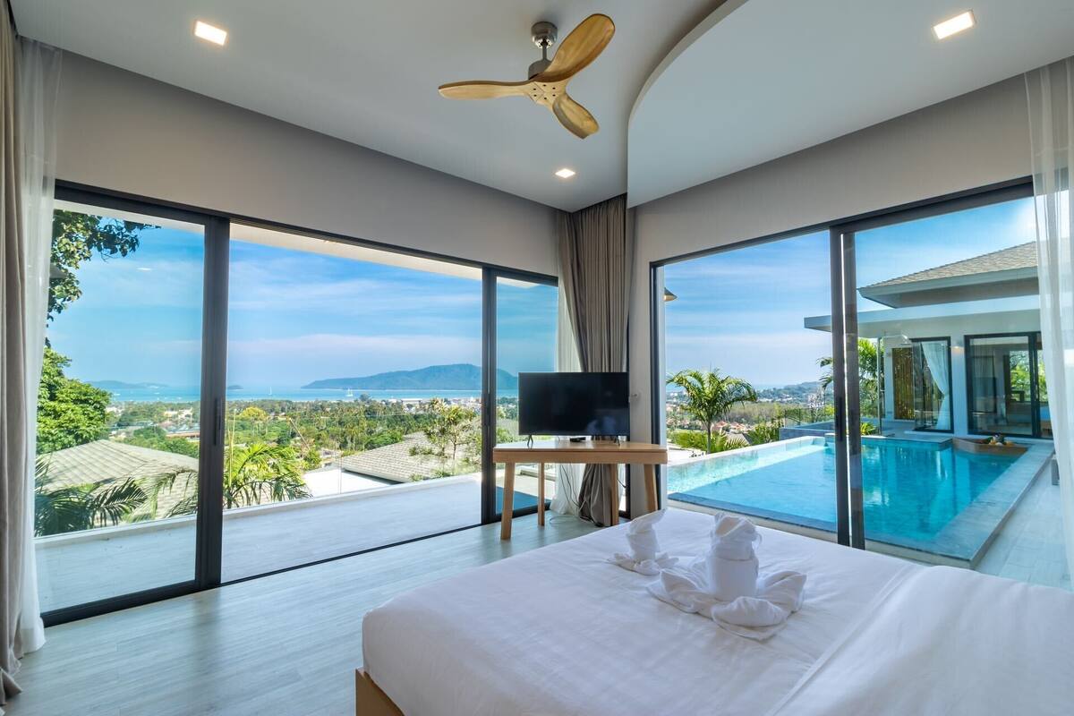 A modern hotel room with a large bed, a TV, and a view of a swimming pool and landscape.
