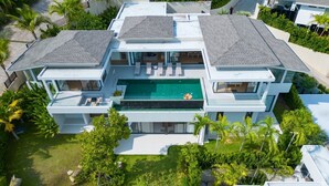 Uma casa moderna de dois andares com piscina no terraço, rodeada por vegetação exuberante e palmeiras.