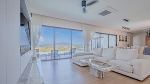 Uma sala de estar espaçosa com um sofá branco grande, uma mesa de centro de mármore e um ventilador de teto.
