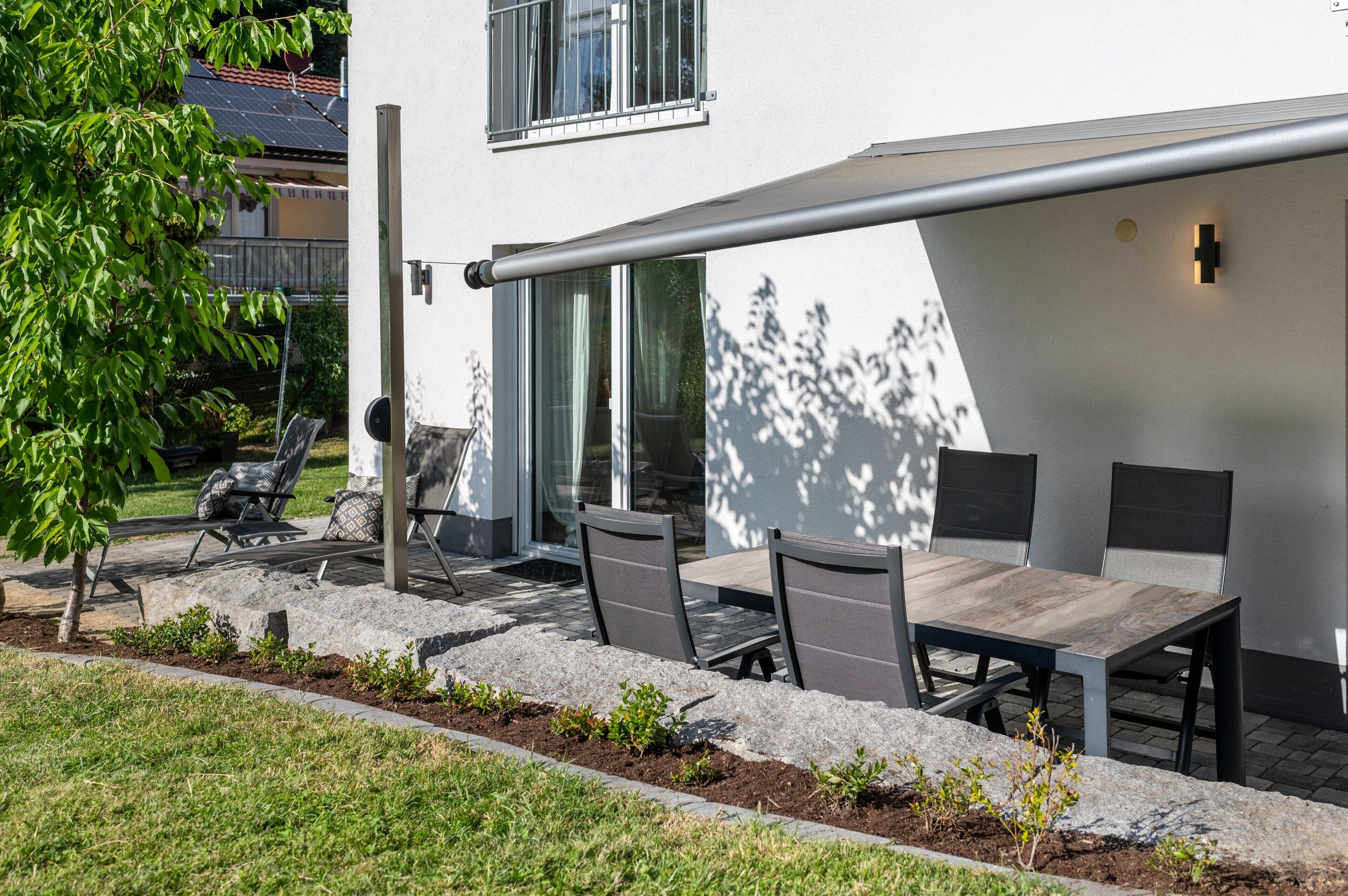 An outdoor patio with a table and chairs, a pergola, and a view of a residential building.