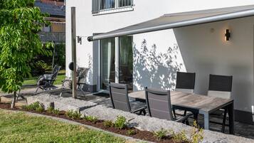 An outdoor patio with a table and chairs, a pergola, and a view of a residential building.