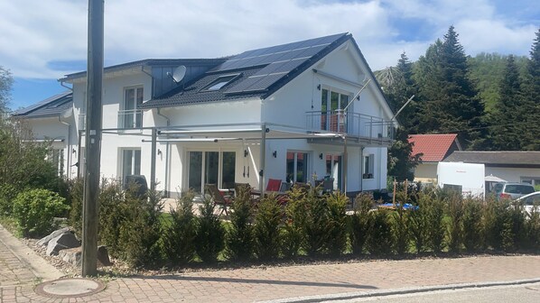 Une maison à deux étages dotée d’un balcon, de panneaux solaires et d’un patio couvert.