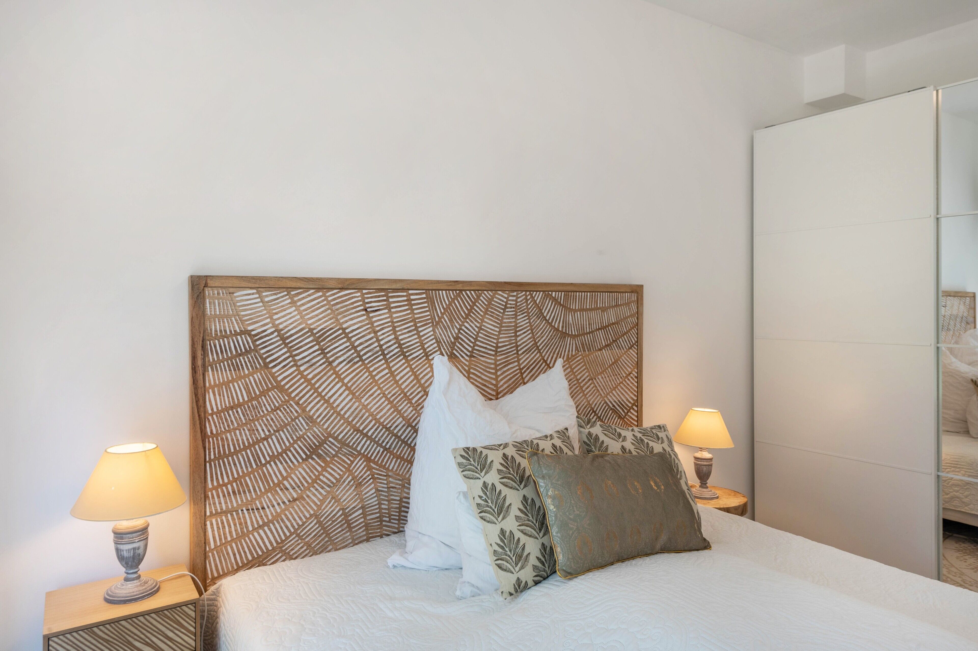 Una cama con un cabecero estampado, dos lámparas de noche y un espejo en la pared.