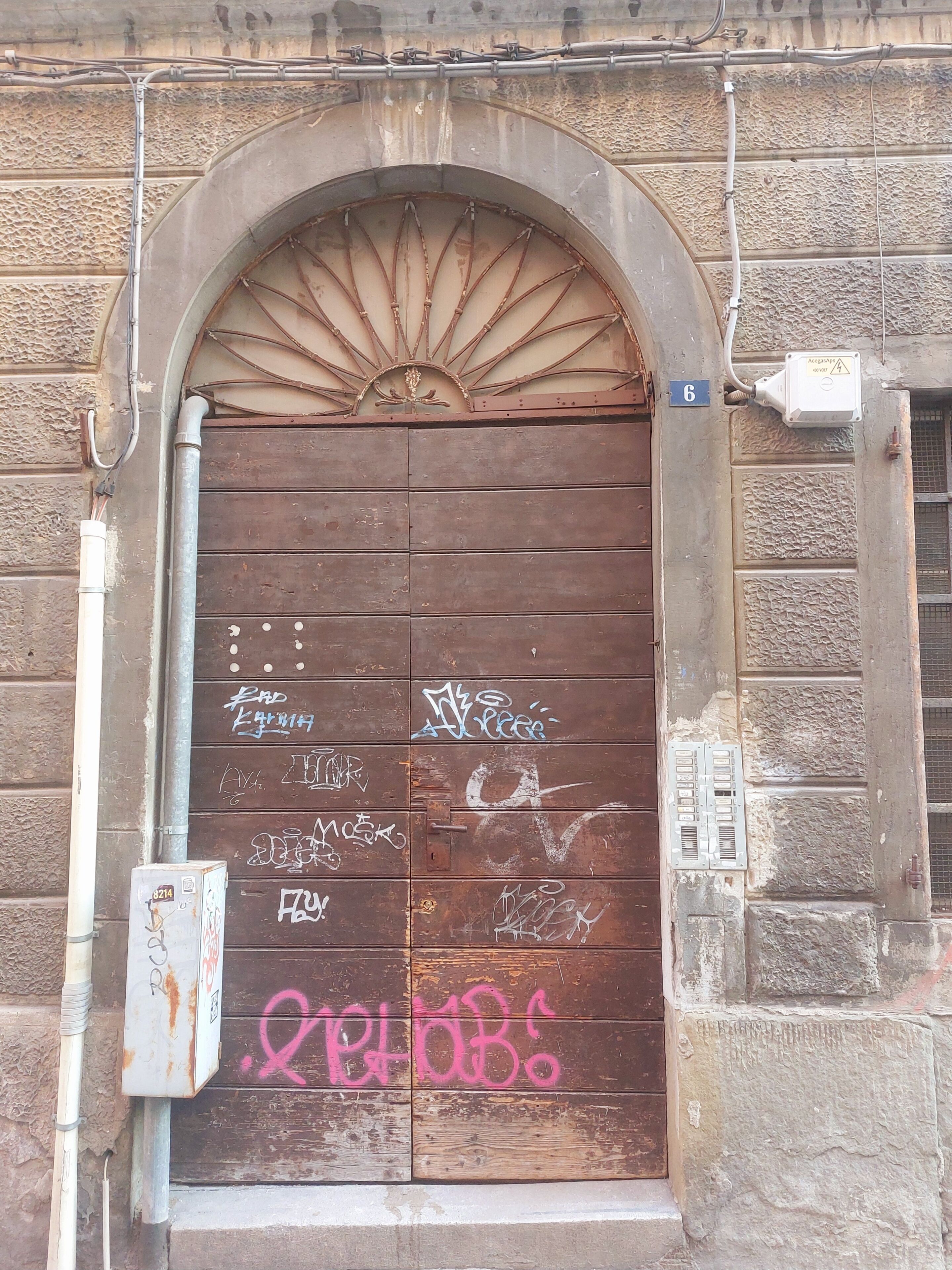 A weathered wooden door with graffiti, a metal pipe, and a utility box.