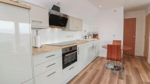 Una cocina moderna con armarios blancos, horno empotrado y microondas. Hay una encimera de madera y una zona de comedor con una mesa redonda y dos sillas.