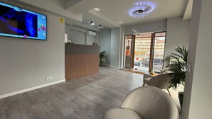A modern reception area with a flat-screen TV, a reception desk, and a large sliding glass door leading to an outdoor area. - At Georges Stay & Fly (Otopeni)