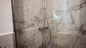Ducha con puerta de cristal y pared de mármol.