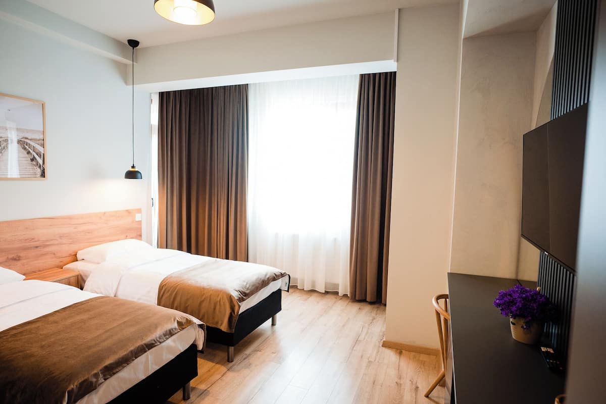 Quarto de hotel com duas camas, televisão e janela com cortinas.