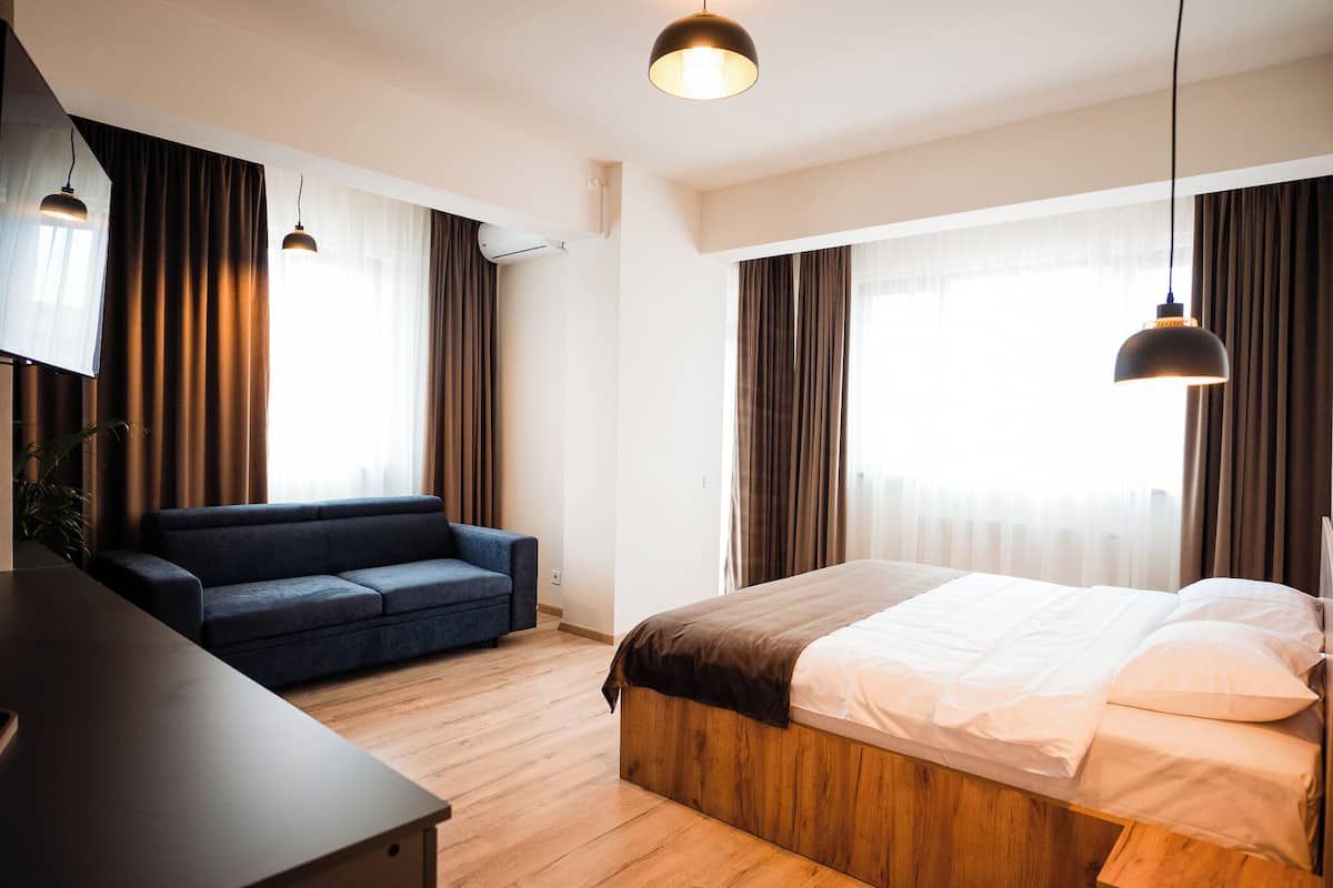 Quarto de hotel moderno com cama de madeira, sofá azul escuro e escrivaninha de madeira.