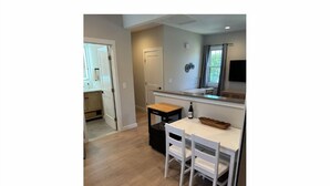 A compact kitchen with a white countertop, a small wooden table, and a TV mounted above it.