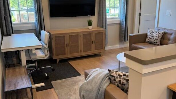 A modern living room with a flat-screen TV, a dining table, a sofa, and a small kitchen area.