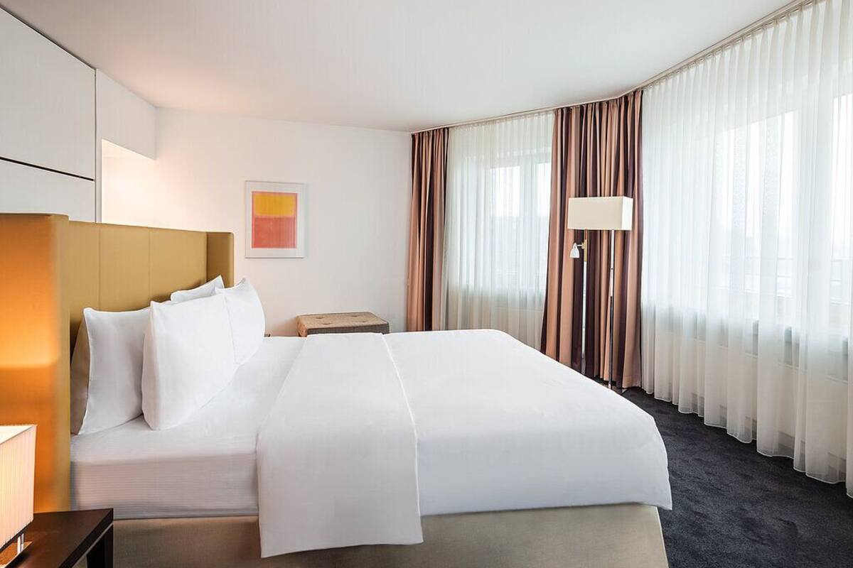 Een hotelkamer met een groot bed, een nachtkastje, een lamp en een raam met gordijnen.