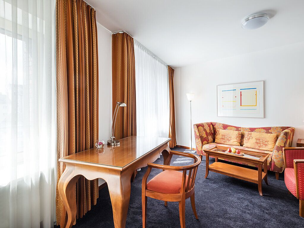 Una habitación de hotel con un escritorio de madera, una silla, un sofá y una lámpara.