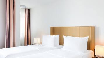 Hotellihuone, jossa on kaksi sänkyä, sängynpääty, yöpöydät lampuineen ja ikkuna, jossa on verhot.