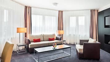 Ein modernes Hotelzimmer mit einer Couch, Sesseln, einem Couchtisch und einem Fernseher.