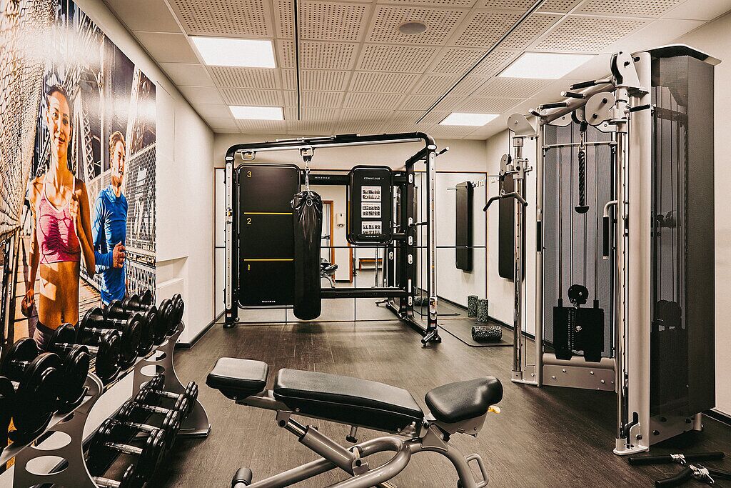 Ein Fitnessraum mit Gewichthebern, Bänken und einer Wand mit Motivationspostern.