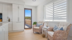 A modern kitchen with white cabinets, a dining area with wicker furniture, and a view through a glass door.